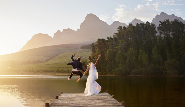 Bride and groom holding hands and jumping in a mountain lake together